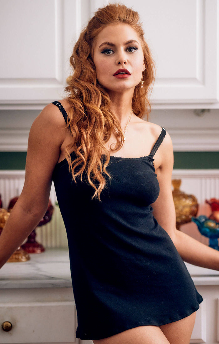 Redhead model wears cute, sexy black cotton chemise nightie with dotted diamond pointelle and bust style lines with sweet satin bows and white picot elastic in playful loungewear pinup style for comfy relaxation